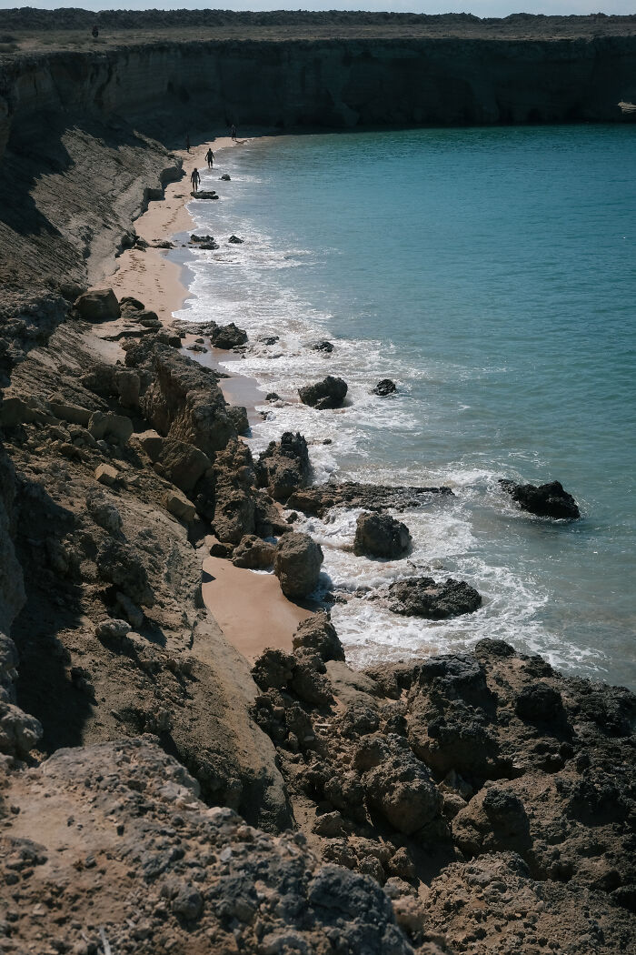 A rocky coastline with people walking along the shore of the Strait of Hormuz, revealing its human presence.