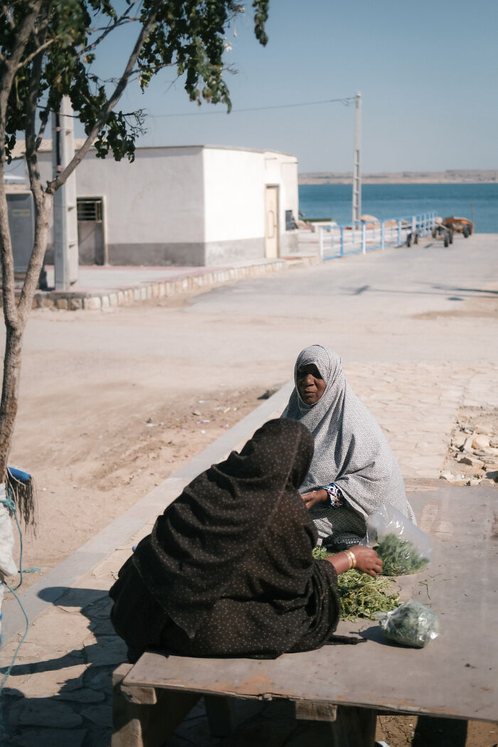Two women in traditional attire selling produce by the Strait of Hormuz, depicting the human side of the hotspot.
