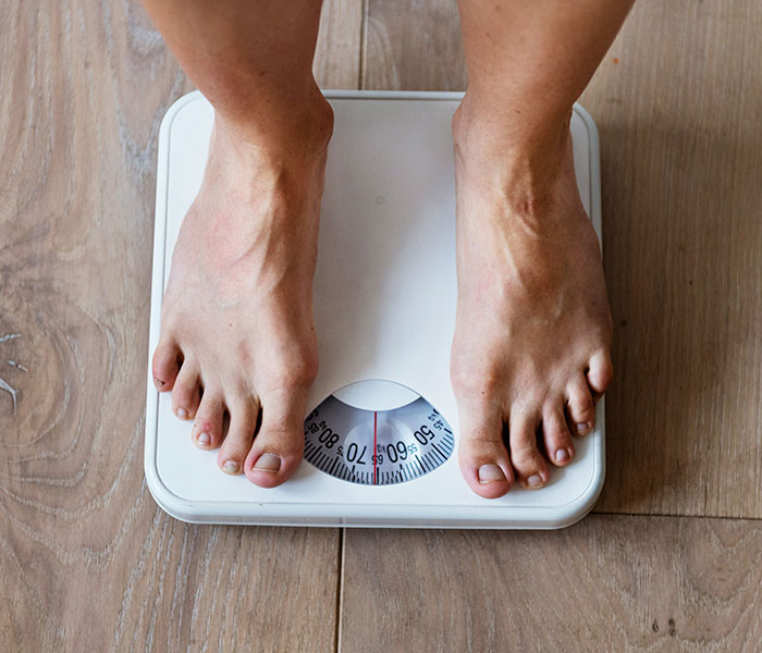 Feet on a weighing scale, representing weight loss, a key cancer symptom that people often dismiss as normal. Feet on a weighing scale, representing weight loss, a key cancer symptom that people often dismiss as normal.