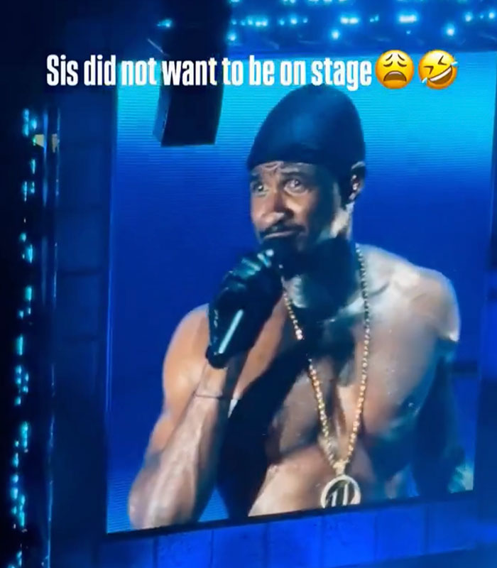 Usher, shirtless and wearing a beanie, singing into a microphone on stage, looking intense.