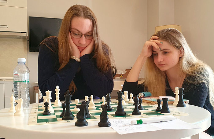 Two members of an all-female chess team deeply engrossed in a game, reflecting on their next moves. Two members of an all-female chess team deeply engrossed in a game, reflecting on their next moves.