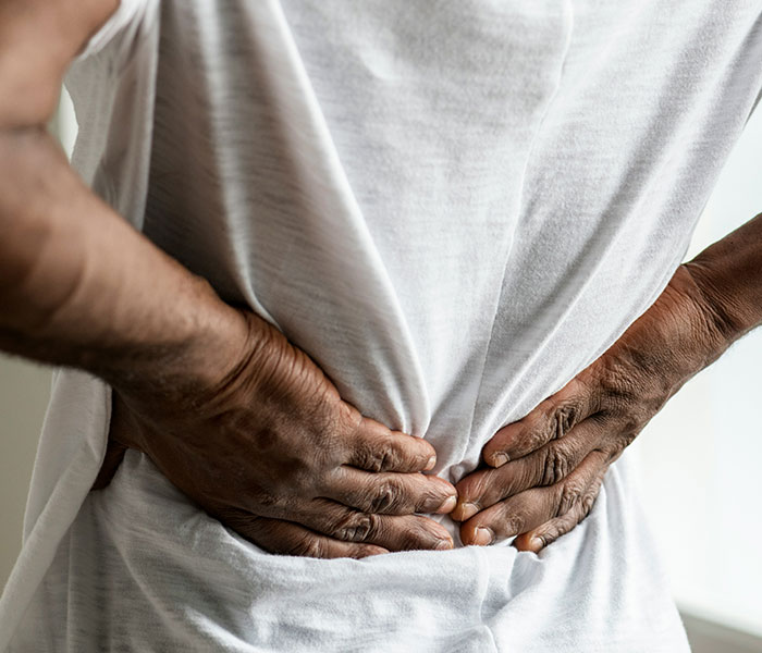 A person holding their lower back, illustrating back pain as a cancer symptom people often dismiss as normal aging. A person holding their lower back, illustrating back pain as a cancer symptom people often dismiss as normal aging.
