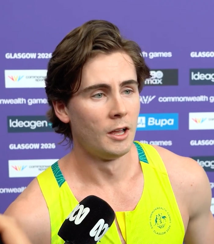 Male athlete in a yellow Australian team uniform speaking into a microphone, discussing the Commonwealth Games wardrobe fail.