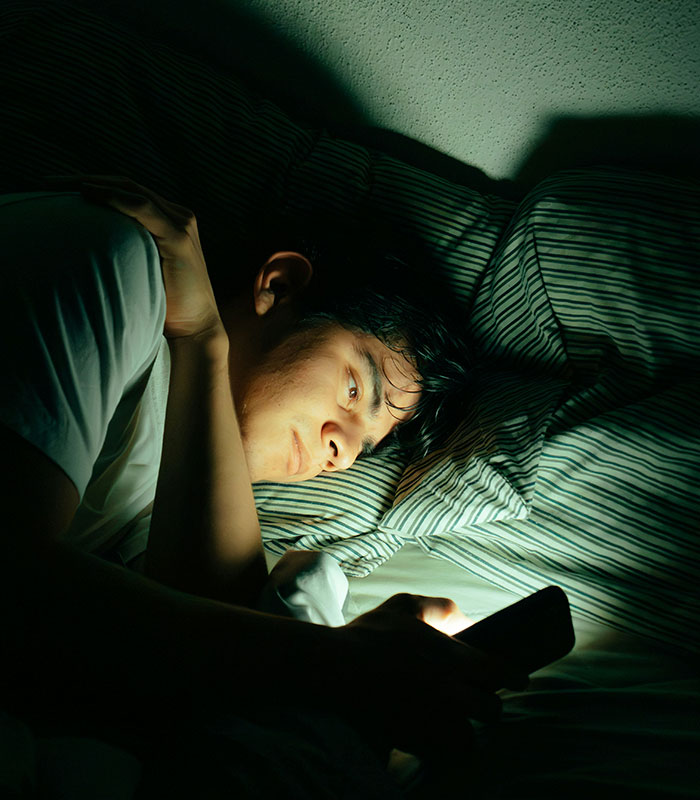 A person looking at a phone in bed at night, highlighting morning habits that could be damaging health and cortisol. A person looking at a phone in bed at night, highlighting morning habits that could be damaging health and cortisol.