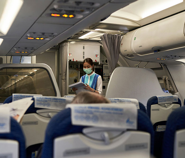 A flight attendant wearing a face mask standing in an airplane aisle, emphasizing flights and turbulence. A flight attendant wearing a face mask standing in an airplane aisle, emphasizing flights and turbulence.