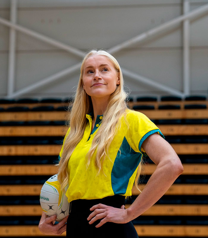 Female athlete sprint star holding a ball, posing against a backdrop of seats.