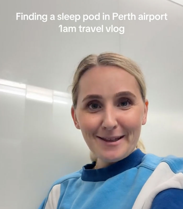 A smiling woman in a blue and white sweatshirt, recording a travel vlog about airport sleeping pods. A smiling woman in a blue and white sweatshirt, recording a travel vlog about airport sleeping pods.