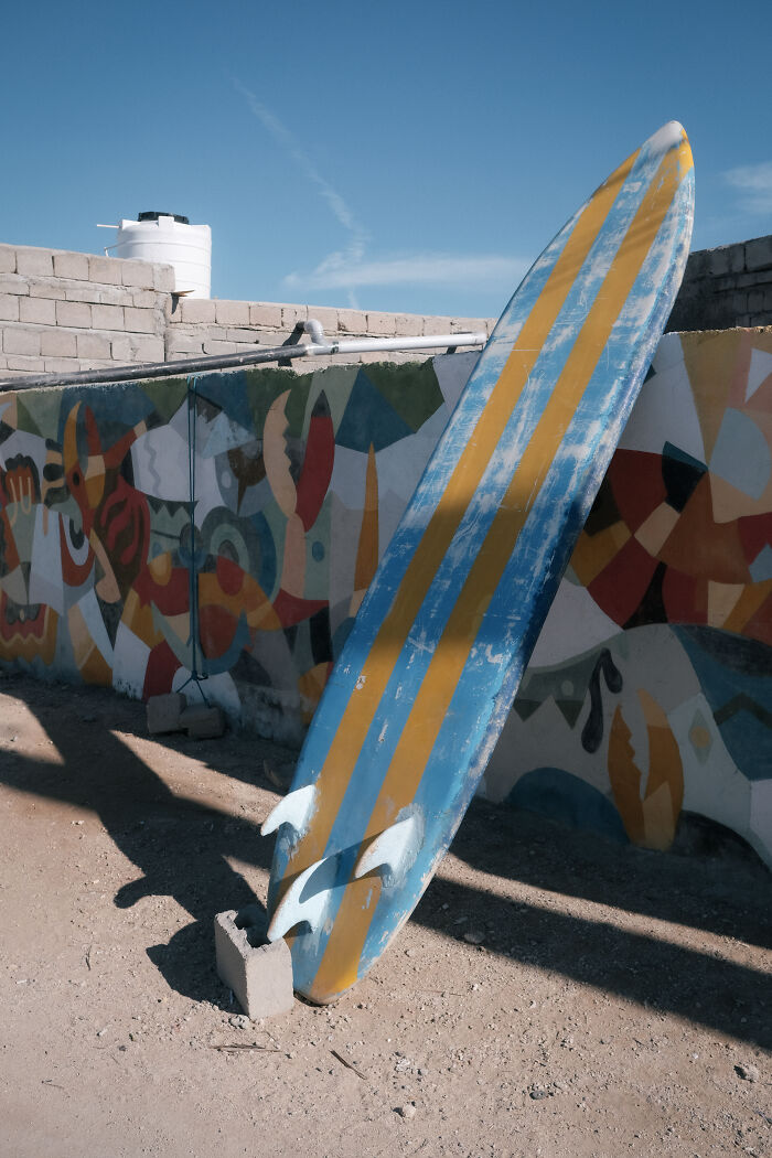 A blue and yellow surfboard leaning against a colorful wall, highlighting the human side of Strait of Hormuz.