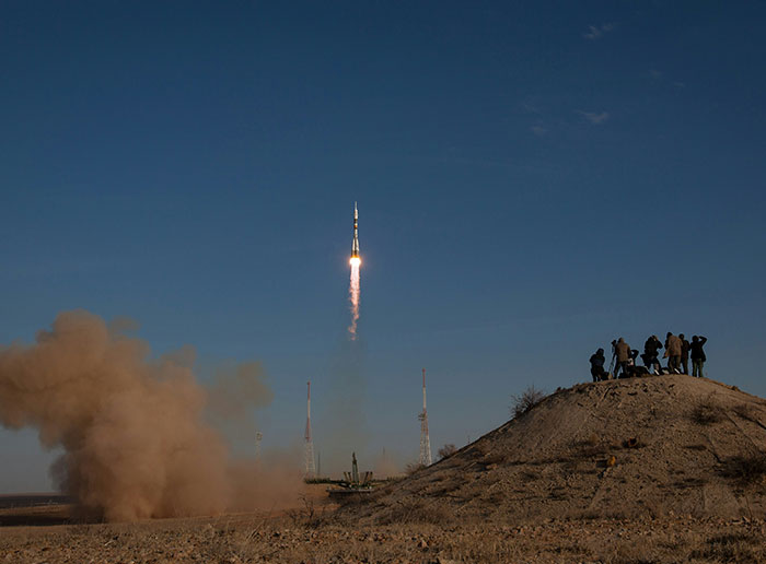 A rocket launching into a clear sky, with observers on a hill, relating to NASA, photos, and potential alien presence.