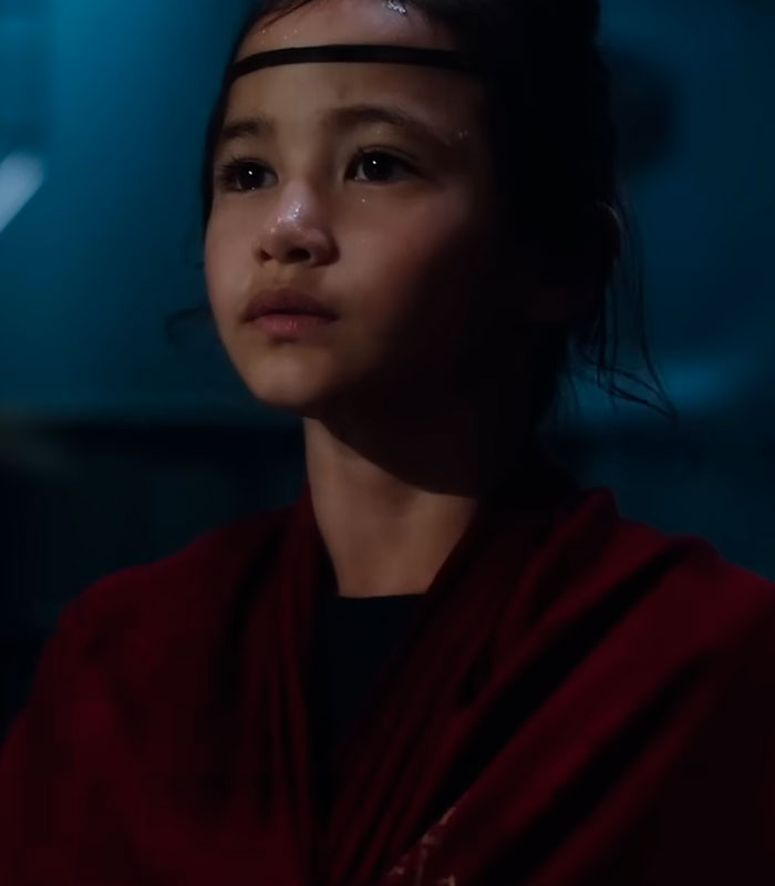 Godzilla actress Kaylee Hottle, with a headband and red fabric, gazes upward in a somber expression. Godzilla actress Kaylee Hottle, with a headband and red fabric, gazes upward in a somber expression.