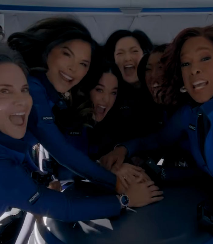 Katy Perry and a group of women in blue jumpsuits, celebrating happily together after a bizarre stunt.