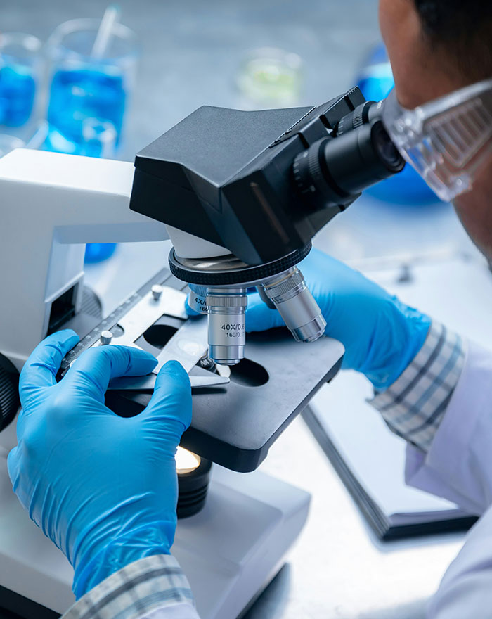 A medical professional with gloves and goggles looking into a microscope, investigating a suspected medical horror story.