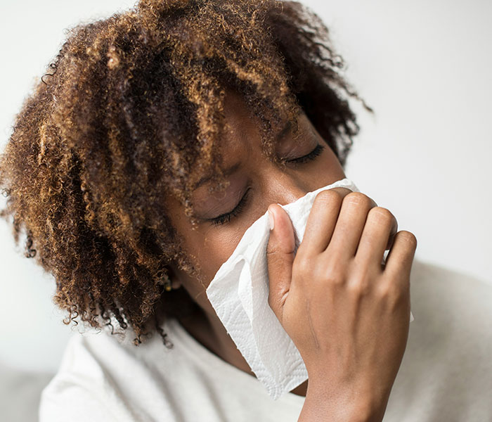Woman blowing her nose, showing a cancer symptom that people often dismiss as normal aging or stress. Woman blowing her nose, showing a cancer symptom that people often dismiss as normal aging or stress.