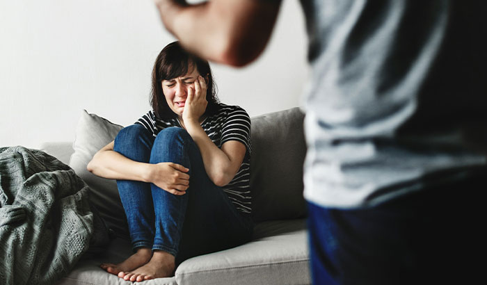 A woman is upset about her fiancé's response and crying on a sofa, with a man standing in the foreground. A woman is upset about her fiancé's response and crying on a sofa, with a man standing in the foreground.