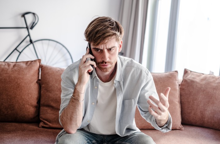 A man looking angry on the phone after a woman walks into her home to see her husband and her sister completely naked.