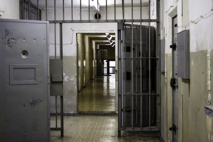 A long, narrow prison hallway with open cell doors and barred windows, illustrating the aunt's jail sentence. A long, narrow prison hallway with open cell doors and barred windows, illustrating the aunt's jail sentence.