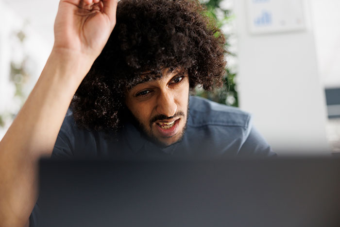 A software engineer looking confused and frustrated at a laptop, experiencing a new hiring scam.