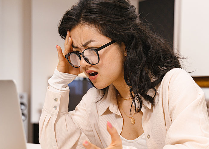 A woman looks frustrated, holding her head, reflecting the feeling of being used by a friend and seeking internet advice.