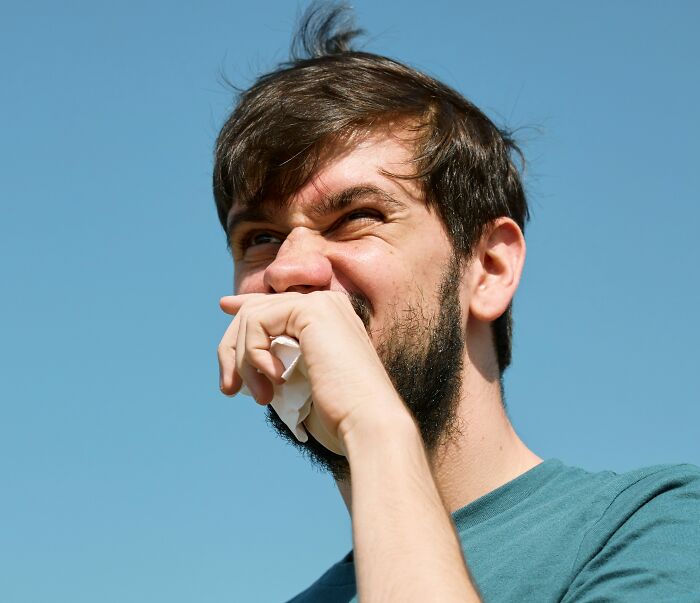 A man sneezing into a tissue with a blue sky background, an image for curious facts about health.