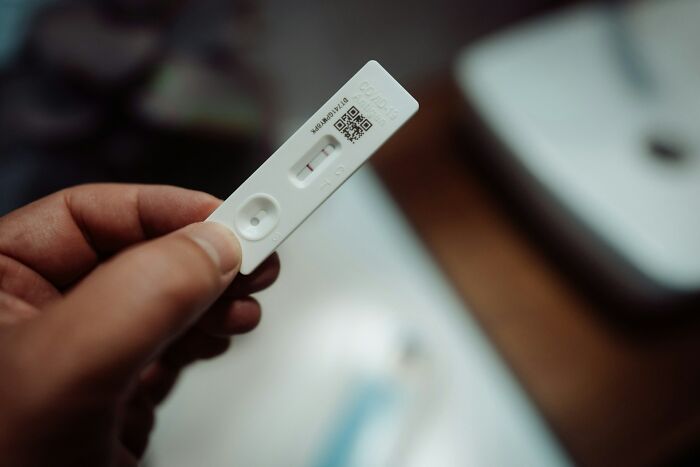 A hand holding a white COVID-19 rapid antigen test strip with a positive result, a curious fact of modern times.