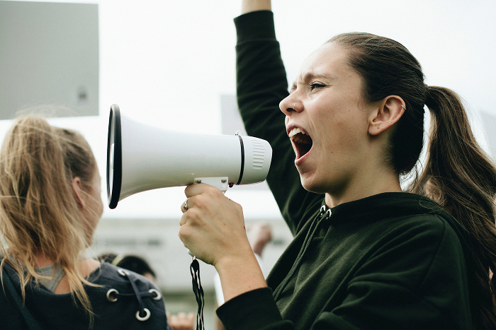 A woman yells into a megaphone during a protest, representing strong reactions to infuriating mansplaining examples.