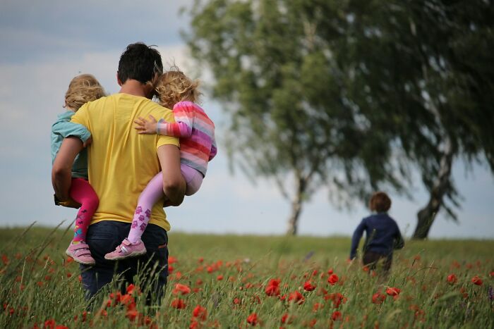 A man carrying two small children in a field of red flowers. Hilarious micro feminism clap backs.