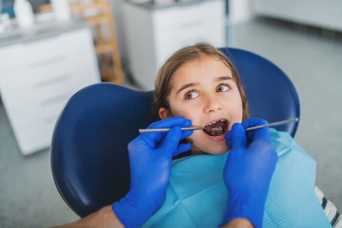 A young girl in a dental chair with a dentist examining her mouth, a common scenario for questions kids ask.