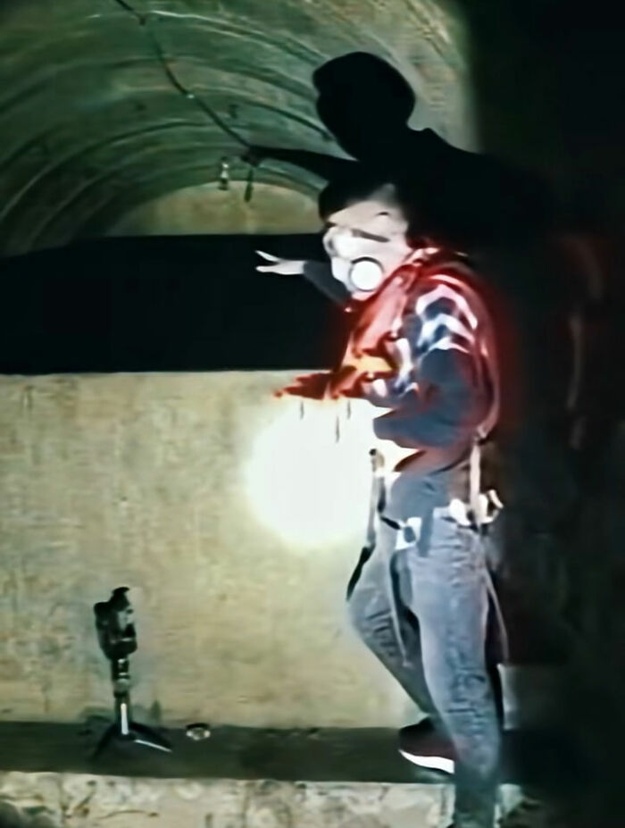 A person wearing a gas mask and holding a flashlight in a dark, underground tunnel, exploring an unsolved mystery.