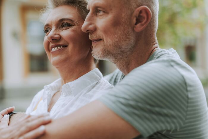 An older couple embracing outdoors, looking content, representing an age-gap relationship.
