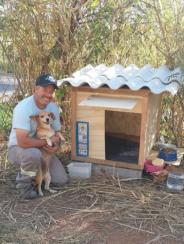 A truck driver from Brazil kneeling beside a completed dog shelter, holding a small dog, for animals in need. A truck driver from Brazil kneeling beside a completed dog shelter, holding a small dog, for animals in need.