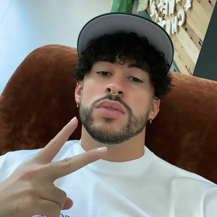 Bad Bunny looking at the camera wearing a hat and white shirt, making a peace sign, fans lose it. Bad Bunny looking at the camera wearing a hat and white shirt, making a peace sign, fans lose it.
