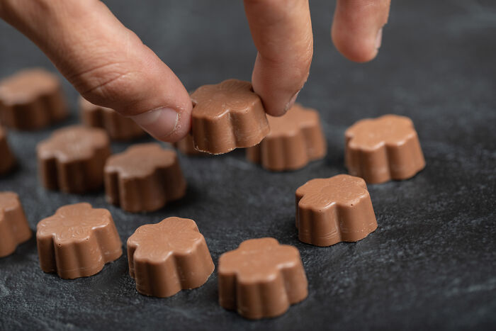 A hand picking up a small chocolate candy, symbolizing sweet moments contrasting with regrettable weddings.