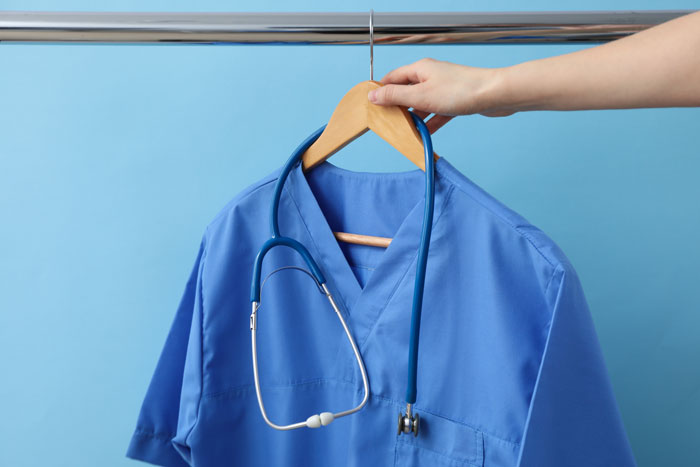 A hand holding a hanger with blue medical scrubs and a stethoscope, symbolizing a spouse's career impacting a divorce lawyer situation.