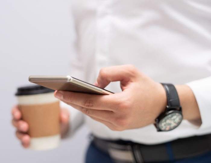 A person holding a phone and coffee, taking a break from work, possibly contemplating to quit job due to infuriating boss stories.