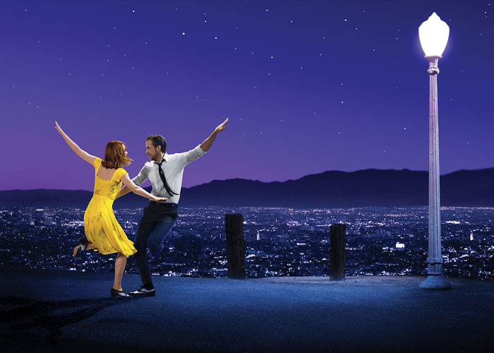 Ryan Gosling and Emma Stone dancing under a street lamp with a city skyline in the background, a scene from the movie.