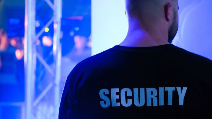 The back of a man's black shirt with the word SECURITY printed in light blue, indicating protection and order.