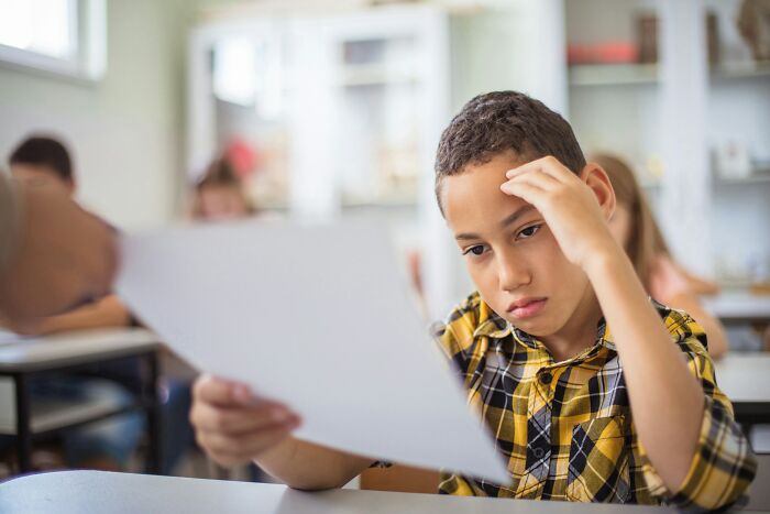 A worried Gen Alpha student in a classroom receiving a test paper, reflecting teachers' grim picture of school.
