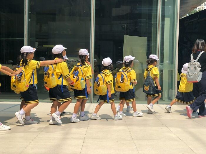 A line of Gen Alpha students in matching uniforms and hats walking outside. Teachers paint a grim picture.