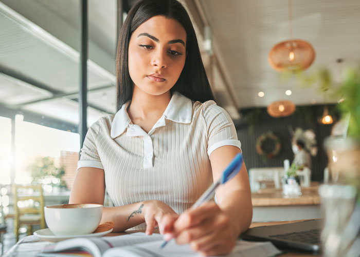 A woman writing in a notebook at a cafe, focused on hard truths that women learned.