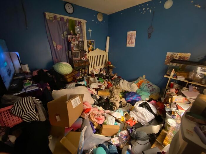 A very messy room with clothes, boxes, and items scattered everywhere, showing men freaked out by a woman's home.