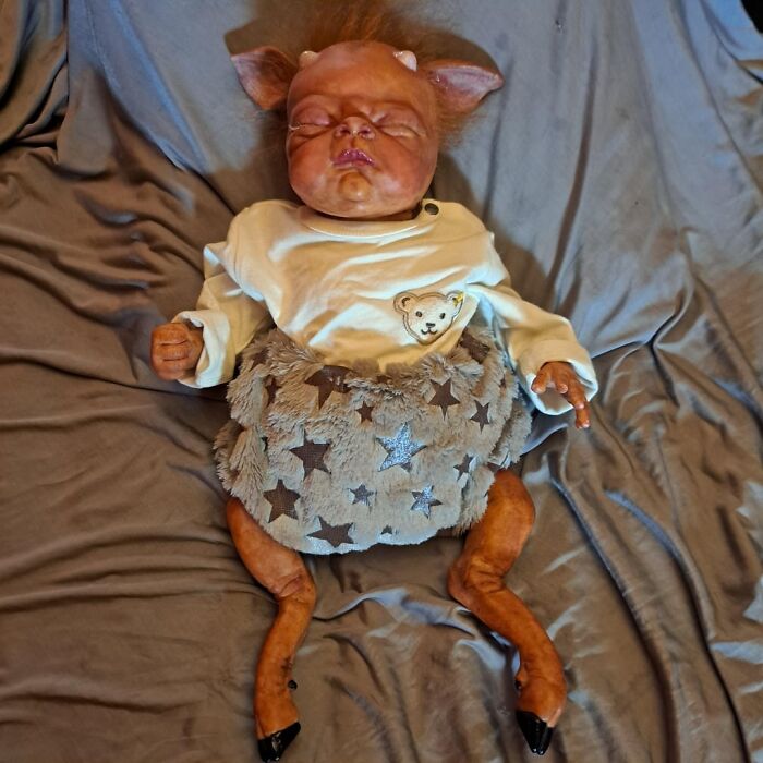A creepy baby doll with animal-like features on a gray blanket. Men freak out.