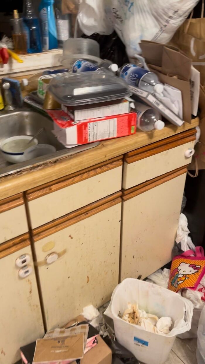 A very dirty kitchen counter with a sink and cabinets, covered in trash and dishes. Men freak out.