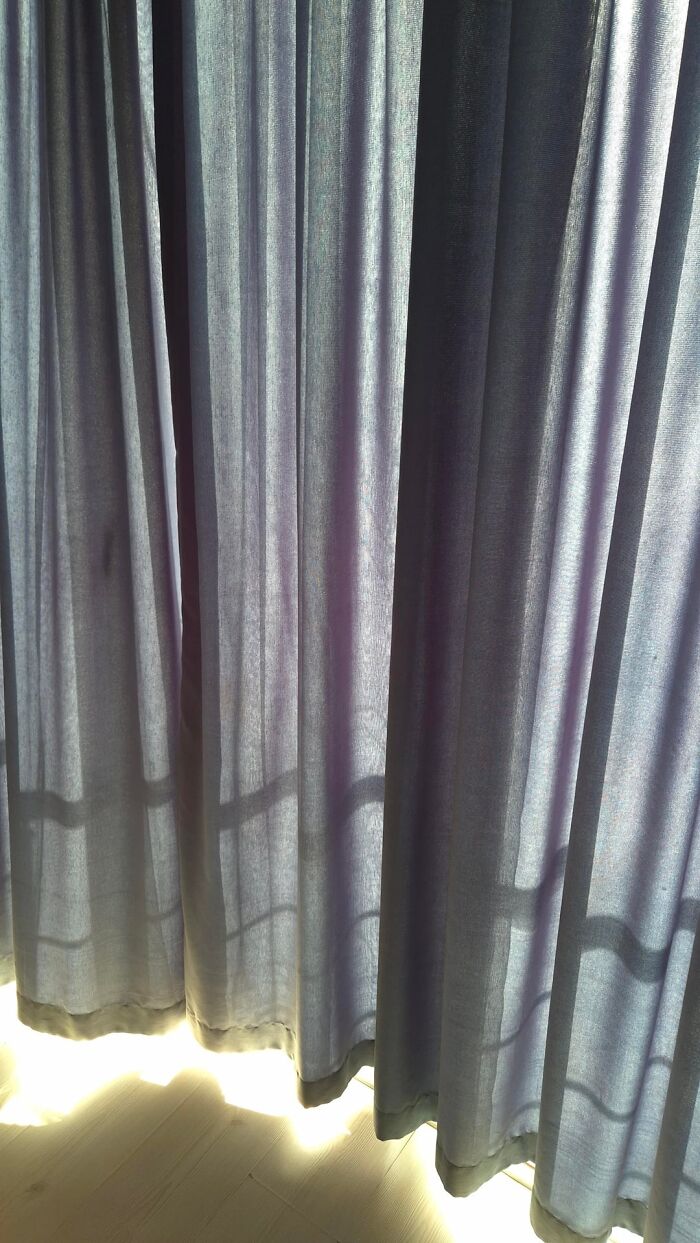 Sunlight shining through translucent blue curtains in a woman's home, creating a freaky shadow pattern.