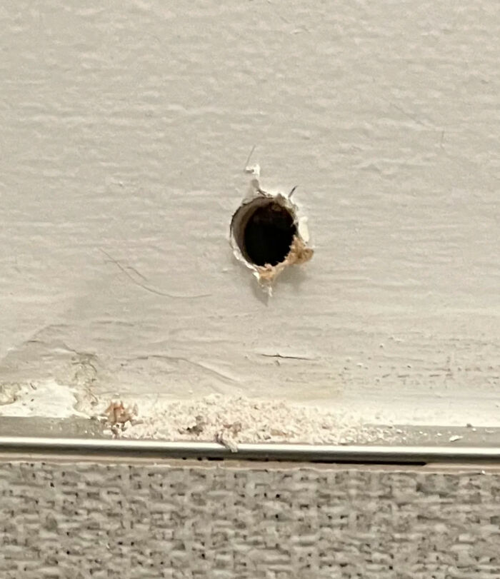 A large hole freaked out a man in a wall near a light switch and remote control in a woman's home.