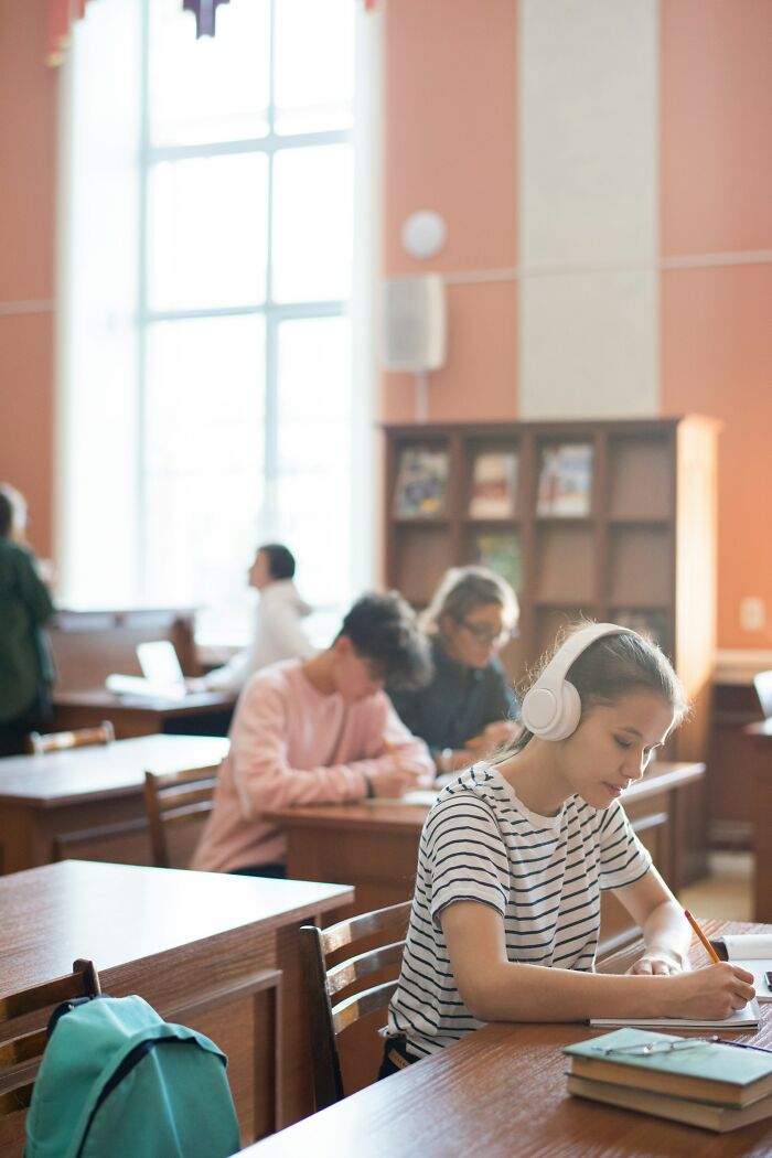 A student in a classroom, wearing headphones and taking notes, representing Gen Alpha at school.
