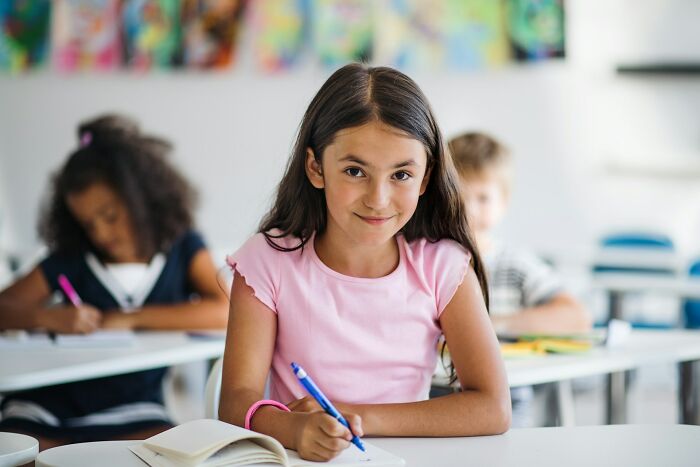 A young Gen Alpha girl smiling while writing in a notebook in class, showcasing Gen Alpha at school.