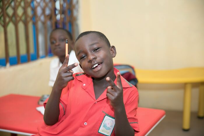 A young Gen Alpha student holding a pencil and making peace signs, depicting Gen Alpha at school.
