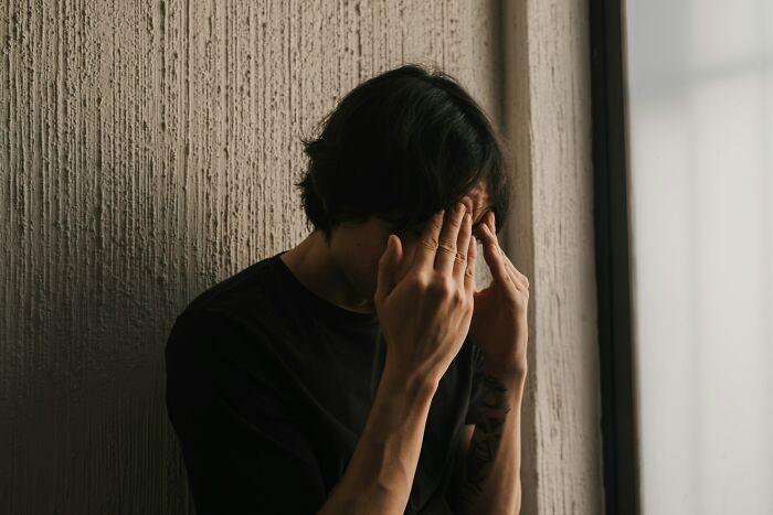 Man holding his head, experiencing depressing or messy thoughts, leaning against a textured wall.