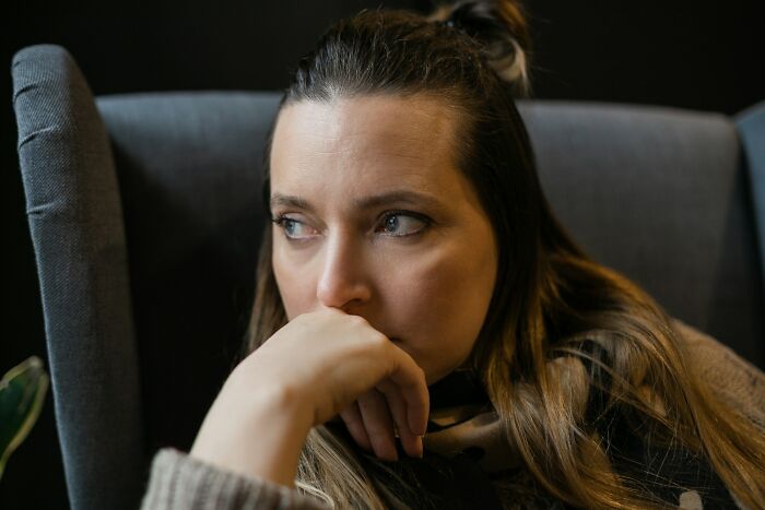 Woman looking worried, contemplating deep secrets or depressing thoughts, in a grey armchair.