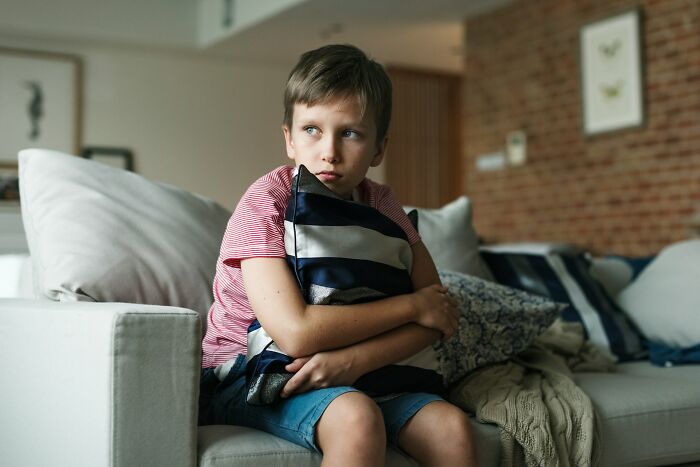 A young boy looking sad and withdrawn while hugging a pillow on a couch, representing a depressing, deep secret.